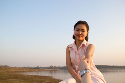Cropped image of woman holding friend hands against lake and clear sky during sunset