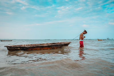 Man with boat in sea against sky