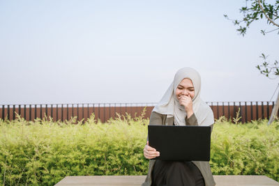 Young woman using mobile phone on field against sky