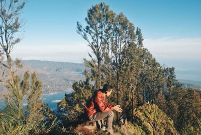 Man sitting on mountain against sky