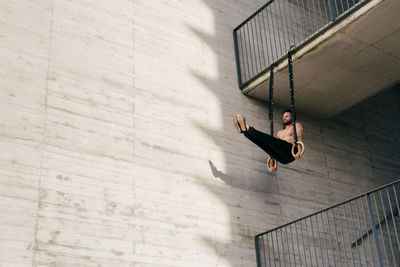 Young shirtless sportsman balancing on gymnastic rings outdoors