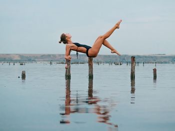 Full length of shirtless young woman in sea against sky