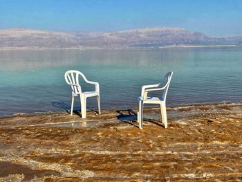 Empty chairs on beach against sky