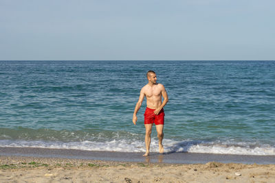 Full length of shirtless man standing at beach against sky