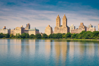 View of buildings by river against cloudy sky