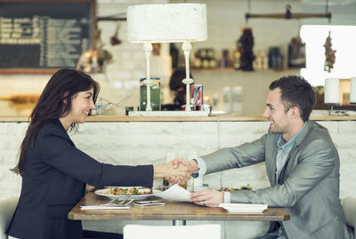 Side view of businessman and businesswoman shaking hands at restaurant table