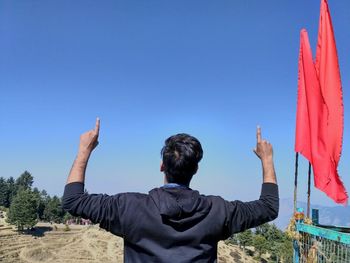 Rear view of man pointing up against clear blue sky