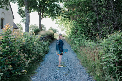 Woman smiling whilst walking down a country lane with her skateboard