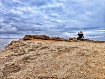 Rear view of man on rock by sea against sky