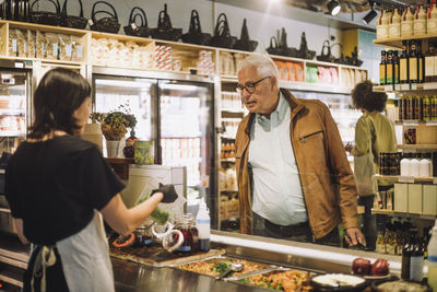 Saleswoman showing container to senior male customer at delicatessen