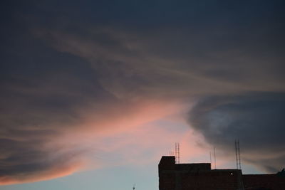 Silhouette factory against sky at sunset