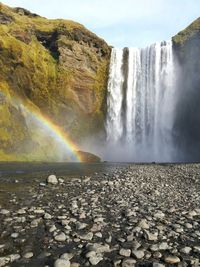 Scenic view of waterfall against rainbow in sky