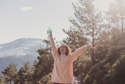 Smiling woman with arms raised looking up while standing on mountain