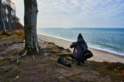 Rear view of woman photographing sea while crouching at beach