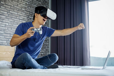 Man using virtual reality simulator while playing video game on bed