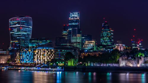 Illuminated cityscape by thames river at night