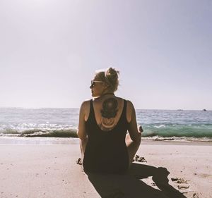Young woman standing on beach against clear sky
