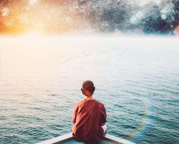 Rear view of man sitting on sea against sky