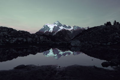 Scenic view of lake by snow covered mountains against sky at dusk