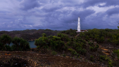Lighthouse amidst plants and buildings against sky