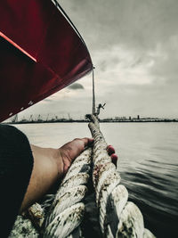 Person holding rope in sea against sky