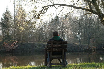 Rear view of man sitting on chair by pond