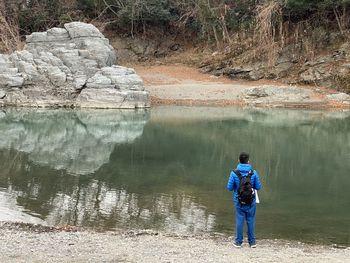 Rear view of man standing on rock by lake