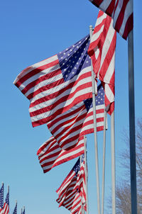 Low angle view of american flags waving against clear blue sky