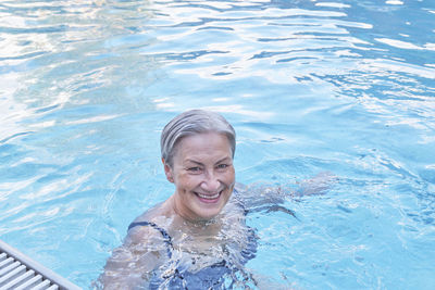 Happy smiling senior caucasian woman with gray hair enjoying in outdoor thermal  pool. 