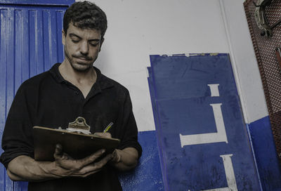 Mechanic in workwear filling in checklist for maintenance and repair service in car station