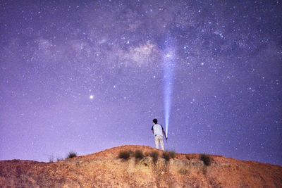 Rear view of man holding illuminated flashlight while standing on land against sky at night