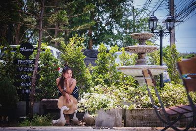 Young woman sitting on plant against trees