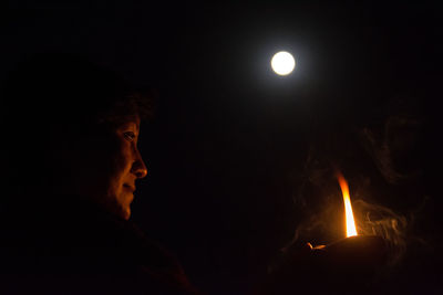 Low angle view of person holding diya against moon at night