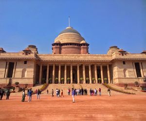 People in front of historical building against clear blue sky