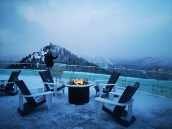 Chairs on snow covered mountain against sky at dusk