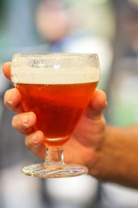 Human hand holding a glass full of red beer