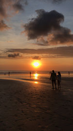 Silhouette people on beach against sky during sunset