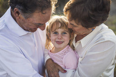 Close up portrait of grandparents hugging granddaughter, funny faces