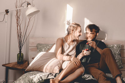 Couple having strawberry while sitting on bed at home
