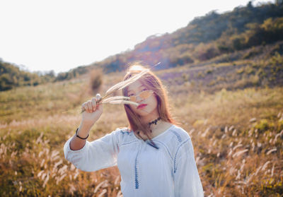 Portrait of woman holding crops while standing on field