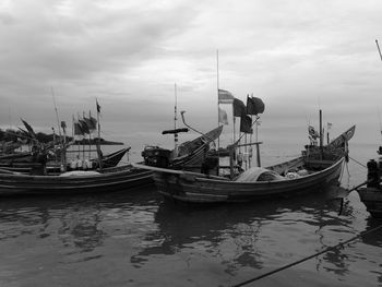 Boats moored in calm sea against cloudy sky