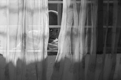 Portrait of boy peeking through window at home