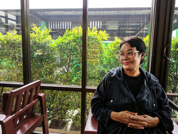 Senior woman looking away while sitting against window