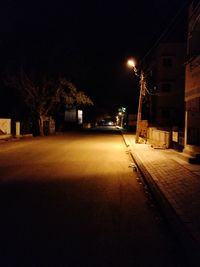 Empty road along illuminated buildings at night