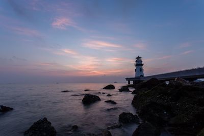 Lighthouse by sea against sky during sunset