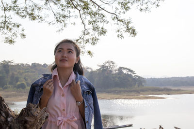 Beautiful young woman standing by lake against clear sky