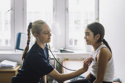 Side view of female healthcare worker listening to patient's heartbeat in clinic