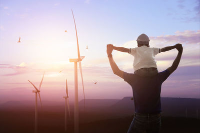 Rear view of man with arms raised standing against sky during sunset