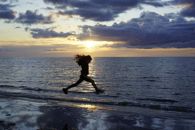 Silhouette man jumping in sea against sky during sunset