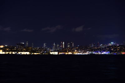 Illuminated cityscape by sea against sky at night